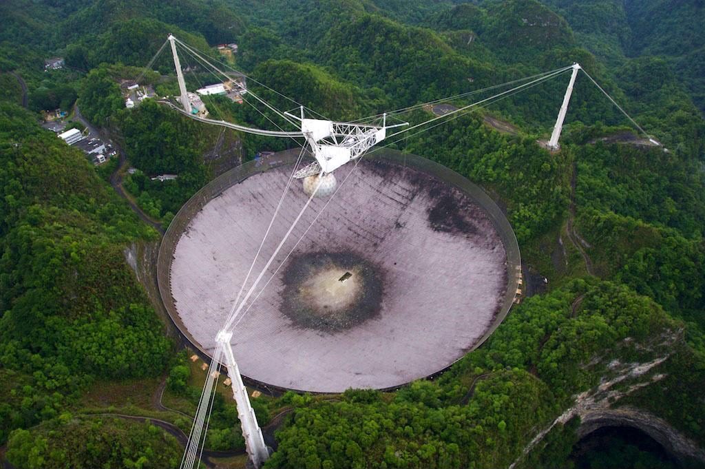 Photo aérienne de l'antenne géante du radiotélescope d’Arecibo sur l’île de Porto Rico dans les Antilles. Elle se trouve au milieu de la forêt et le cliché est pris de jour. 