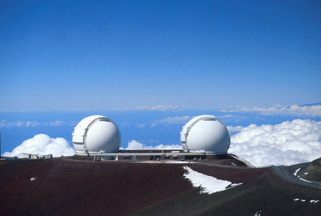 Photo des deux télescopes jumeaux Keck I et II par beau temps, sur le mont Mauna Kea de l'île d’Hawaï. Il surplombent les nuages. 