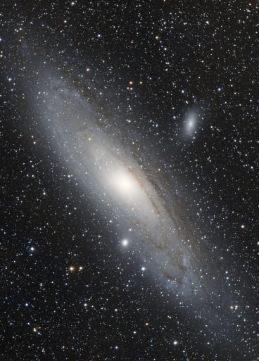 Image de la galaxie M31 dans Andromède. Il s'agit d'un grand ovale nébuleux et lumineux sur un fond de ciel étoilé. On voit deux autres petites galaxies qui l'entourent en haut et en bas.