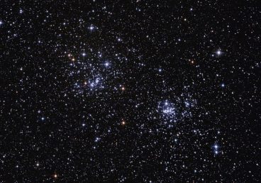 Photo du double amas dans Persée. On voit un fourmillement d'étoiles sur un fond de ciel noir, et au centre deux groupements d'étoiles plus dense. Des étoiles plus brillantes montrent leurs couleurs, bleutées ou orangées.