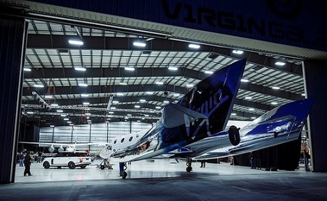 Le vaisseau spatial de Virgin Galactic dans un grand hangar, de nuit.
