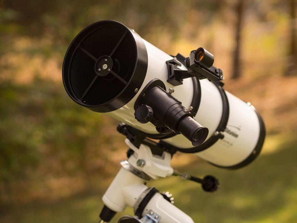 Exemple de télescope Newton. On voit le tube optique de 3/4, le porte-oculaire, le pointeur point rouge et une partie de la monture équatoriale sur un arrière-plan de feuillage.