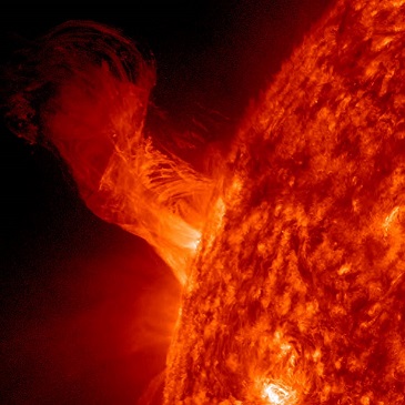 Photographie en couleur rouge intense d'un éruption solaire. On voit une volute de 250 000 km de long environ sortir de la surface du Soleil.