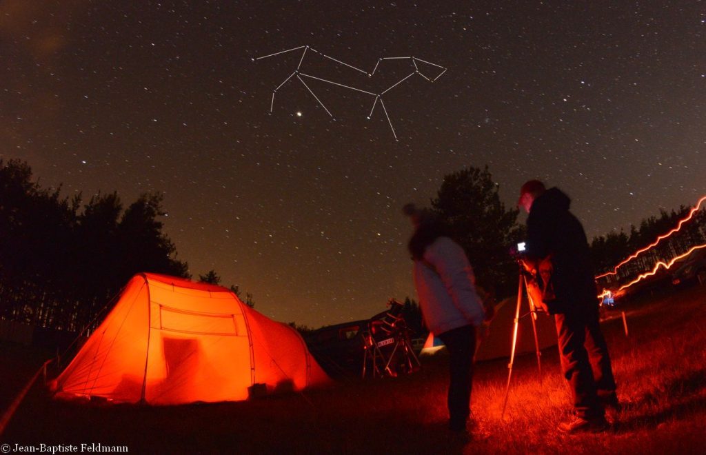 Photo of amateur astronomers observing the starry sky, with the constellation Leo and Jupiter looking like a bright speck of light just above their heads.