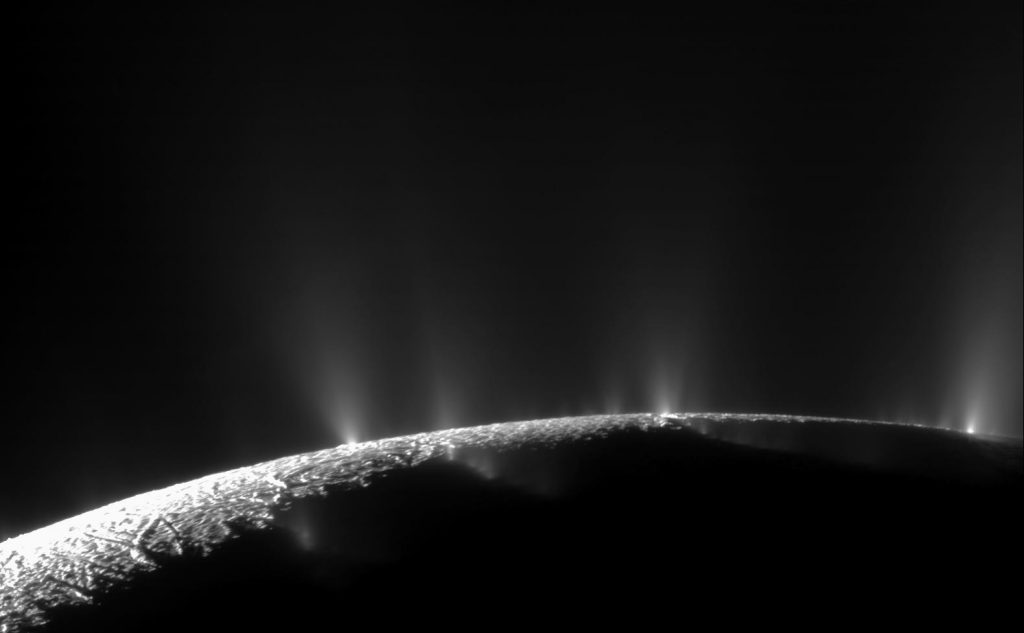 Photo en noir et blanc de la surface d'Encelade, trois geysers gris visibles à l'horizon.