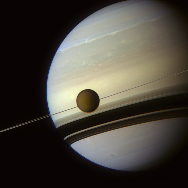 Photo de Saturne par Cassini où l'on voit les anneaux qui ne forment qu'une simple ligne vus par la tranche. Titan est également sur l'image, au même niveau que les anneaux.