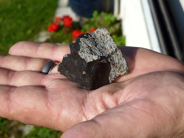 Météorite de couleur noir dans la main d'un chasseur de météorites. Le noir indique que sa chute est récente.