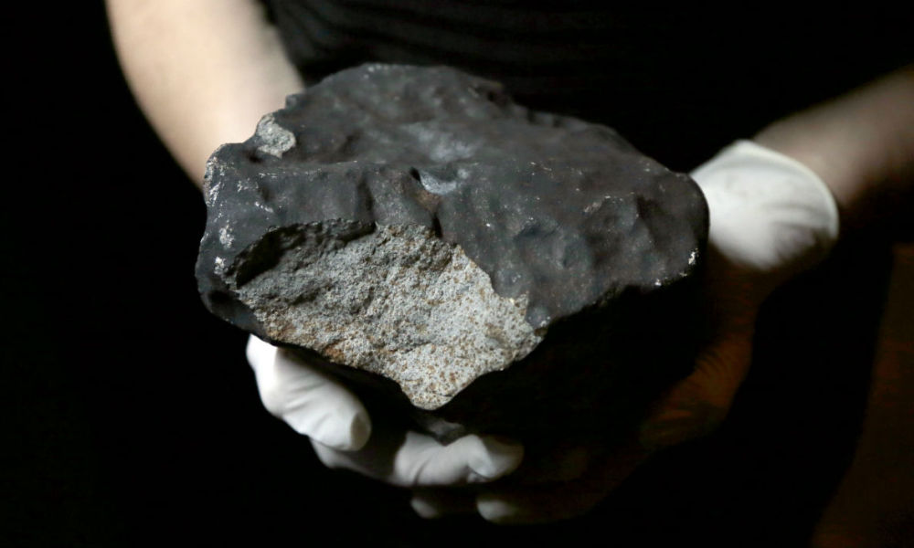 Photo de la plus grosse météorite de France découverte en 2018. Le gros caillou gris anthracite est tenu dans les mains gantées d'un membre du Muséum national d'histoire naturelle de Paris.