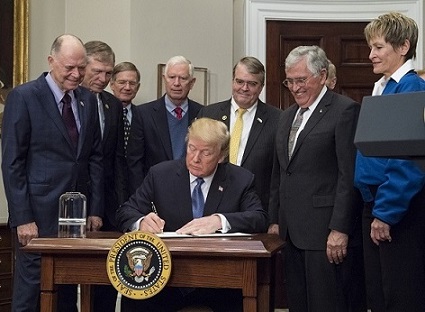 Donald Trump assis à un bureau en train de signer la nouvelle politique spatiale américaine en 2017, entouré par notamment des représentants du Congrès et les astronautes Jack Schmitt et Peggy Whitson.