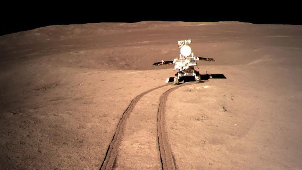 Le rover Yutu-2 à la surface de la Lune. On le voit au bout d'un chemin tracé par ses roues dans le sol lunaire, de couleur rosé. 