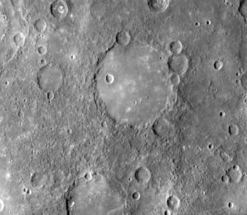 Photo en couleurs grises d'une zone de la surface de Mercure où l'on voit un grand cercle régulier, une plaine lisse, qui illustre un volcanisme passé.