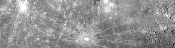 Photo panoramique d'une zone de Mercure : on y voit à sa surface des stries brillantes qui partent en étoile depuis les cratères d'impacts.