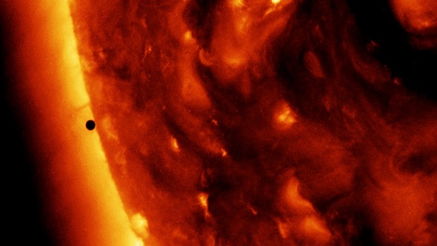 Le Soleil prend toute la partie droite de l'image en couleurs orangé-rouge, tandis qu'un petit cercle noir sur la gauche, proche de la surface du Soleil, correspond à Mercure. 