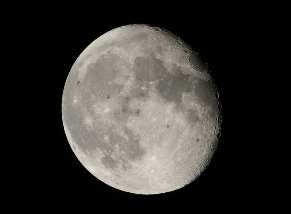 Image de la Lune presque pleine où l'on voit la silhouette de l'ISS à 5 reprises, car il s'agit d'un compositage de 5 images. La Lune est grise, le fond de ciel est noir.