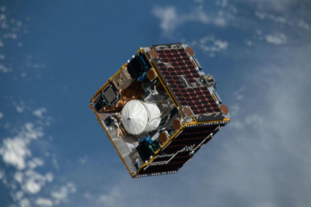 Photo du satellite expérimental RemoveDebris dans l'espace : il est cubique et sur fond bleu (les océans de la Terre)