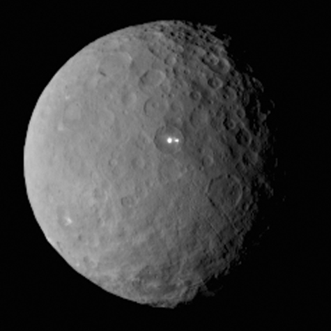 Cérès représentée en entier, d'apparence semblable à la Lune avec beaucoup de cratères et un sol grisé. On voit au centre d'un cratère de l'hémisphère nord deux taches très blanches qui correspondent à de fortes concentrations en sel. 