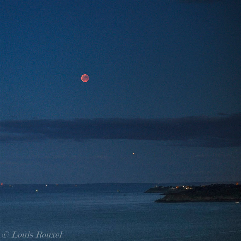 Photo de l’éclipse totale de lune du 27 juillet 2018. On voit la lune orangée qui se lève au dessus de la mer et la planète Mars, orangée aussi, en dessous.