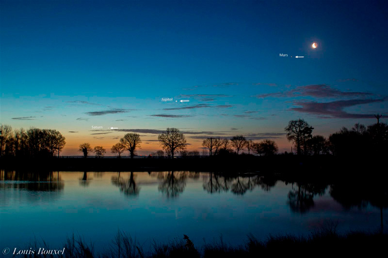 Photo of the Moon, Mars, Jupiter, and Saturn at dawn over a lake. Photo by Louis Rouxel