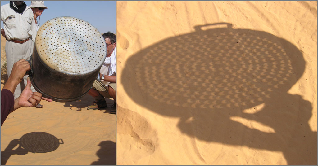 Photo montrant un nomade brandissant un couscoussier pendant l'éclipse de Soleil : l'ombre portée montre des dizaines de petits croissants solaires projetés sur le sable.