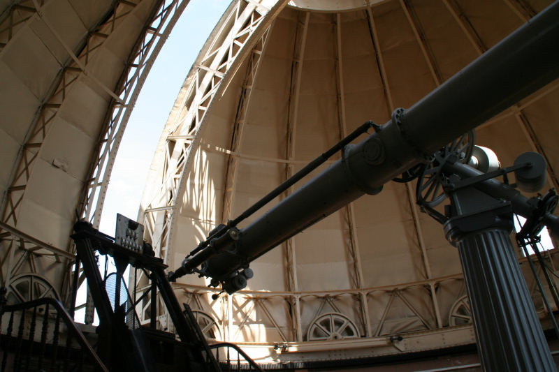 Lunette astronomique de l'Observatoire de Strasbourg sous sa coupole. L'intérieur de la coupole est beige, elle est entre-ouverte et la lunette de couleur gris métallique et dans l'axe de l'ouverture.