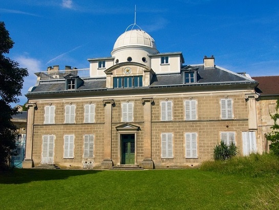 Vue depuis le parc (sol avec de l'herbe verte) de l'Observatoire Camille Flammarion. On voit le bâtiment sur deux étages, grande demeure avec en haut sur le toit une coupole blanche de 5 mètres. 