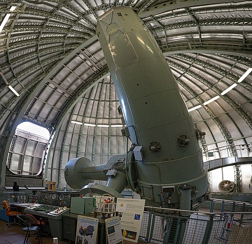 Gros télescope en couleur vert métal de l'Observatoire de Haute-Provence. Il est au centre de l'image sous une coupole d'apparence métallique et est orienté vers le ciel malgré le toit fermé. 