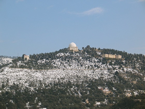 Vue du Mont Gros sur les hauteurs de Nice. De loin, on voit de la végétation provençale et de la pierre blanche, au centre au sommet de la colline une coupole au toit blanc et sur la droite et la gauche un peu en contre-bas des bâtiments en pierres jaunes.