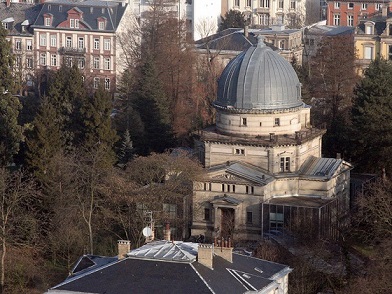 Vue aérienne de la grande coupole de l'Observatoire de Strasbourg. En fond on voit plusieurs immeubles aux briques rouge foncé, et devant le bâtiment en pierres blanches avec les toits dont celui de la coupole de couleur gris clair. 