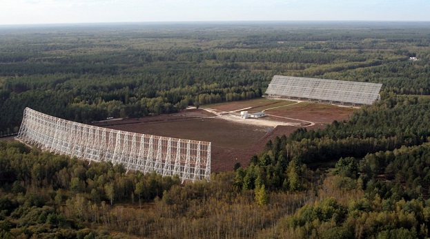 Photo des deux grands miroirs du grand radiotélescope de Nançay face à face. Au milieu de la forêt, dans un champ, deux grands "murs" blancs de 35 et 40 mètres de haut se font face. 