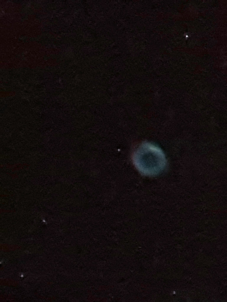 Photo montrant la nébuleuse planétaire de la Lyre, un anneau peu lumineux et légèrement coloré de rouge et de vert.