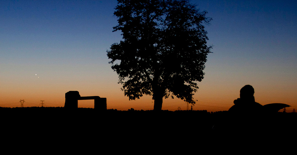 Photo montrant un crépuscule sans nuage. Un observateur et un arbre se découpent en ombre chinoise. A l'horizon, Vénus est brillante et en dessous à droite Jupiter est un peu moins lumineuse.