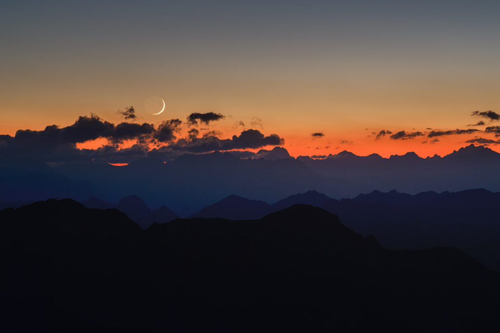 Lune cendrée sur les montagnes du Queyras, quelques nuages habillent l'image. C'est le crépuscule