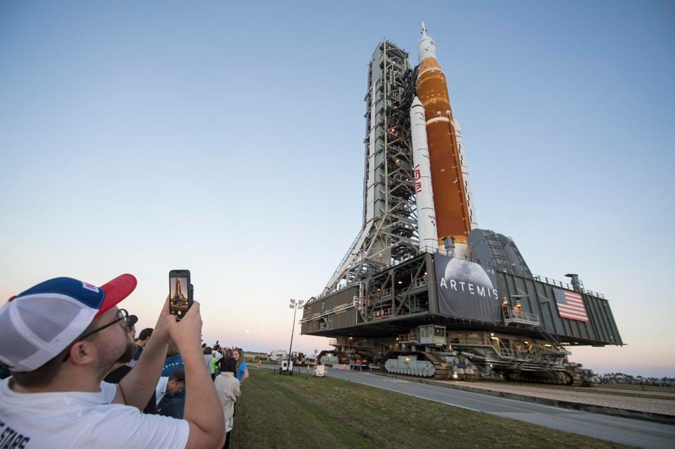 A gauche de l'image un touriste de dos qui prend en photo le lanceur SLS sur la pas de tir du kennedy Space Center, en fin de journée. 