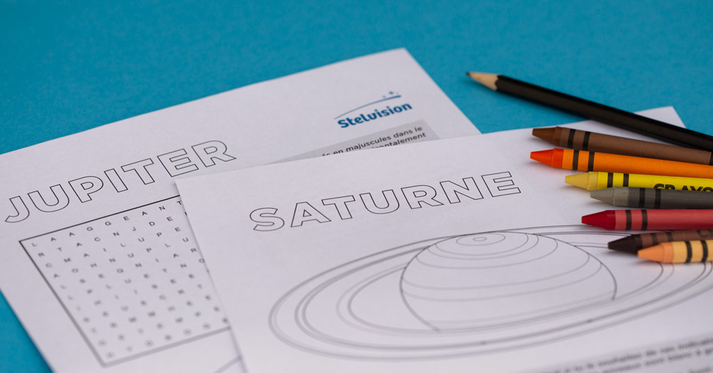 Image montrant des fiches d'activités pour les enfants, thème Jupiter et Saturne. Il y a des crayons de couleur à droite et le fond de l'image est bleu.
