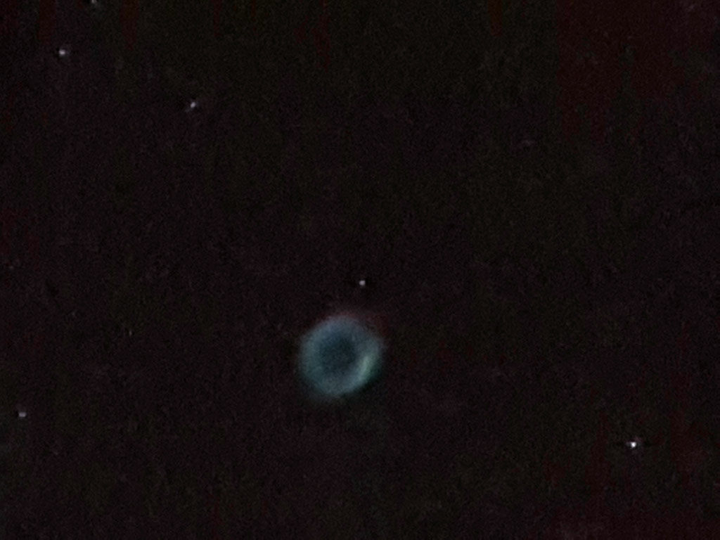 Photo montrant la nébuleuse planétaire de la Lyre, un anneau peu lumineux et légèrement coloré de rouge et de vert.
