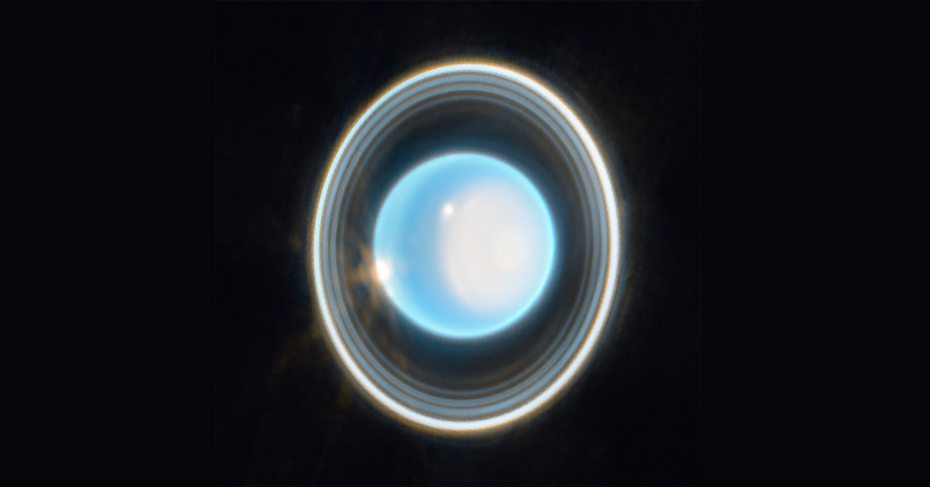 La planète Uranus sur fond noir. La planète apparaît bleu clair avec une grande tache blanche sur le côté droit. Sur le bord de cette tache en haut à gauche se trouve une tache blanche brillante. Un autre point blanc est situé sur le côté gauche de la planète à la position 9 heures. Autour de la planète se trouve un système d'anneaux imbriqués. L'anneau le plus à l'extérieur est le plus brillant tandis que l'anneau le plus à l'intérieur est le plus faible. Contrairement aux anneaux horizontaux de Saturne, les anneaux d'Uranus sont verticaux et semblent donc entourer la planète.
