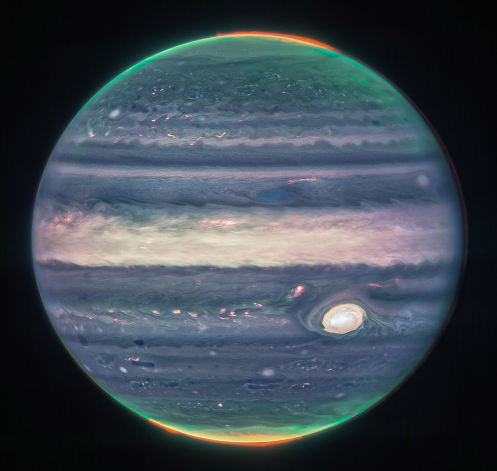 Jupiter domine le fond noir de l'espace. L'image est un composite et montre Jupiter dans des couleurs améliorées, mettant en évidence la grande tache rouge de la planète, qui apparaît ici en blanc. La planète est striée de rayures horizontales tourbillonnantes de turquoise fluo, de pervenche, de rose clair et de crème. Les rayures interagissent et se mélangent sur leurs bords comme de la crème dans le café. Le long des deux pôles, la planète brille en turquoise. Des aurores orange vif brillent juste au-dessus de la surface de la planète aux deux pôles.